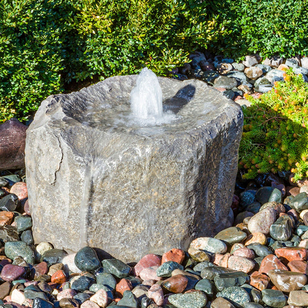 Alder Falls Rock Outdoor Fountain With Small Trees In The Back And Surrounded By Stones