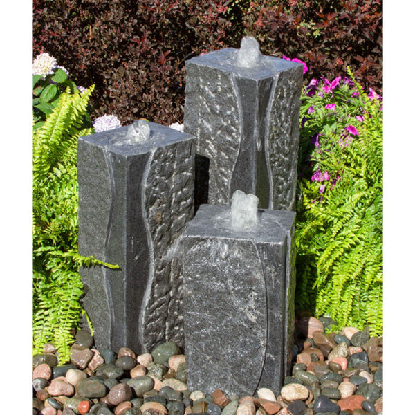 Polished Corner Triple Granite Stone Fountain Surrounded By Ferns And Flowers With Red Trees Behind