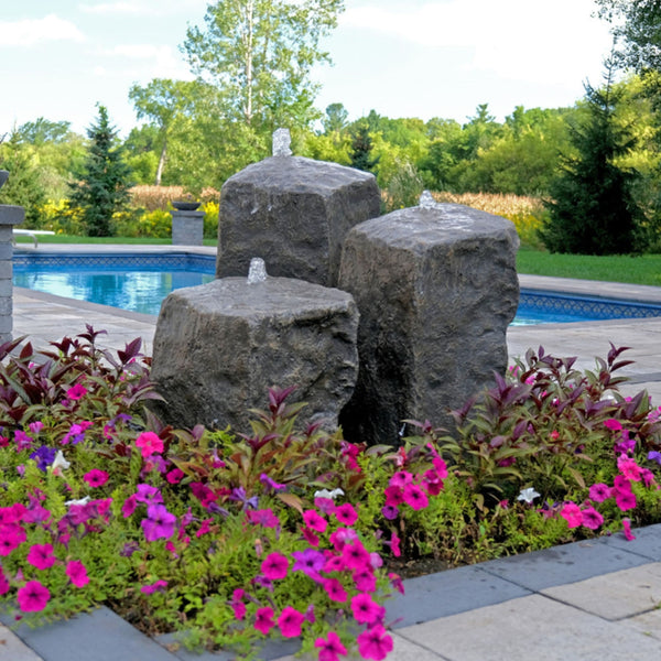 Watershed Triple Rock Outdoor Fountain Surrounded By Colorful Flowers With A Pool In The Background