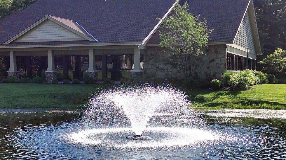Aerating pond fountain spraying a wide plume in front of a lakeside house.