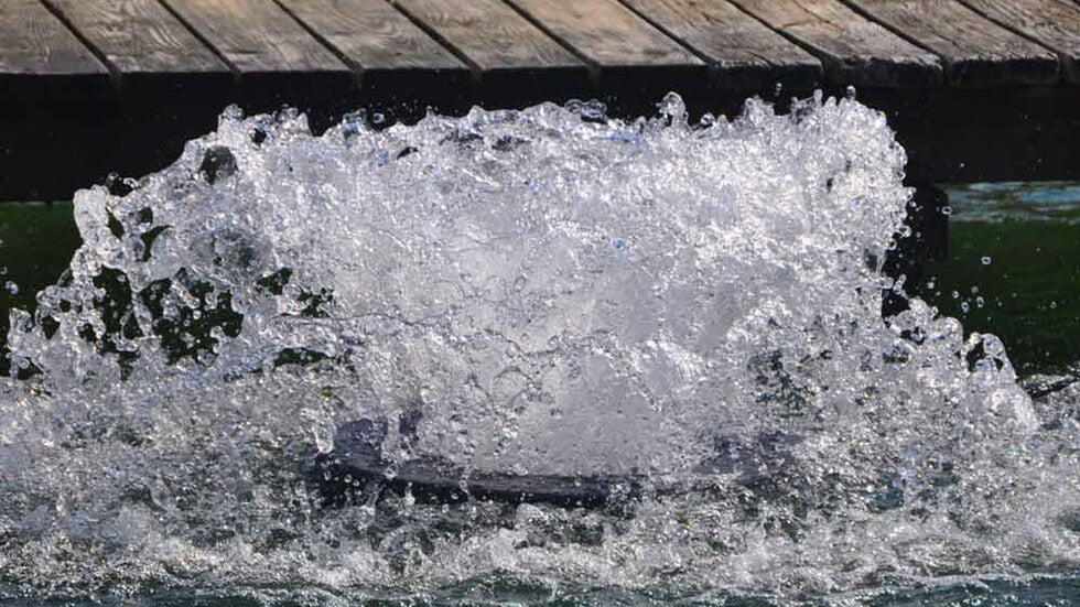 Close-up of a surface aerator creating strong water agitation beside a wooden dock on a pond.