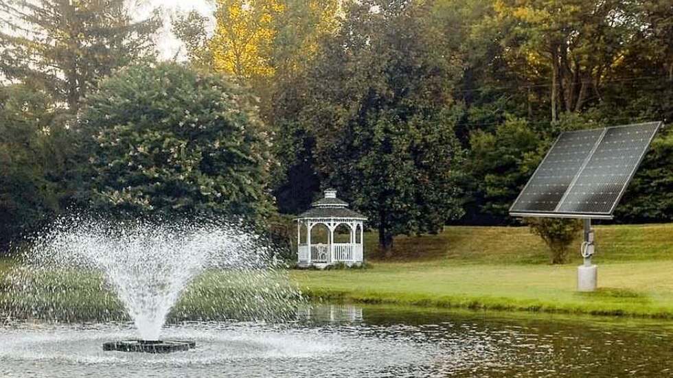 Floating solar-powered pond fountain spraying water, with solar panel on shore