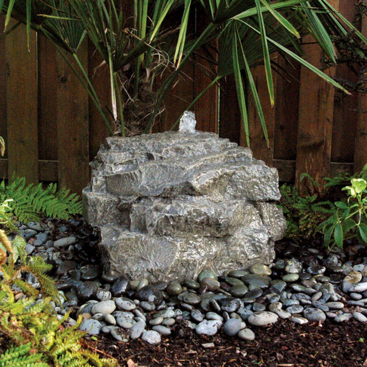 Blue Thumb Mini Mountain Spring stone fountain running in a planted corner against a wooden fence