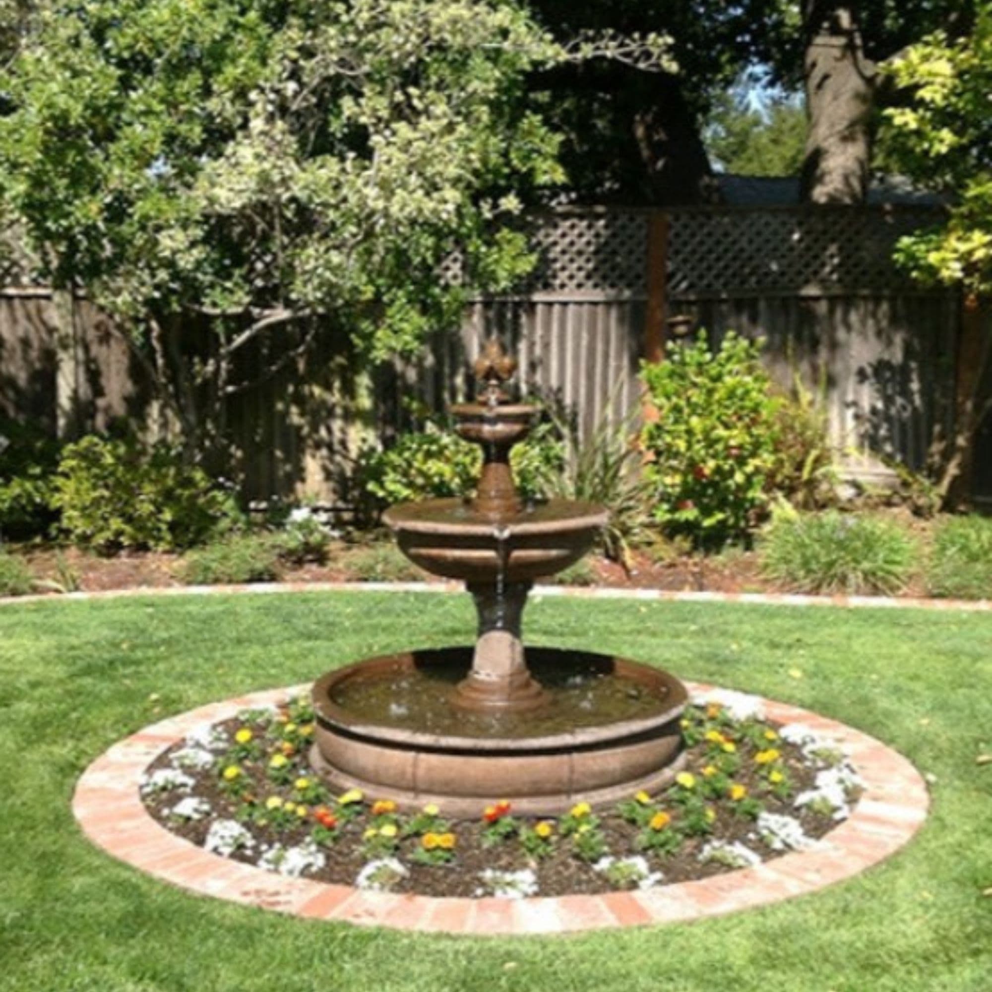 Giannini Garden Fleur De Lis Pond Fountain At Lush Backyard Garden With Fence And Trees In The Background