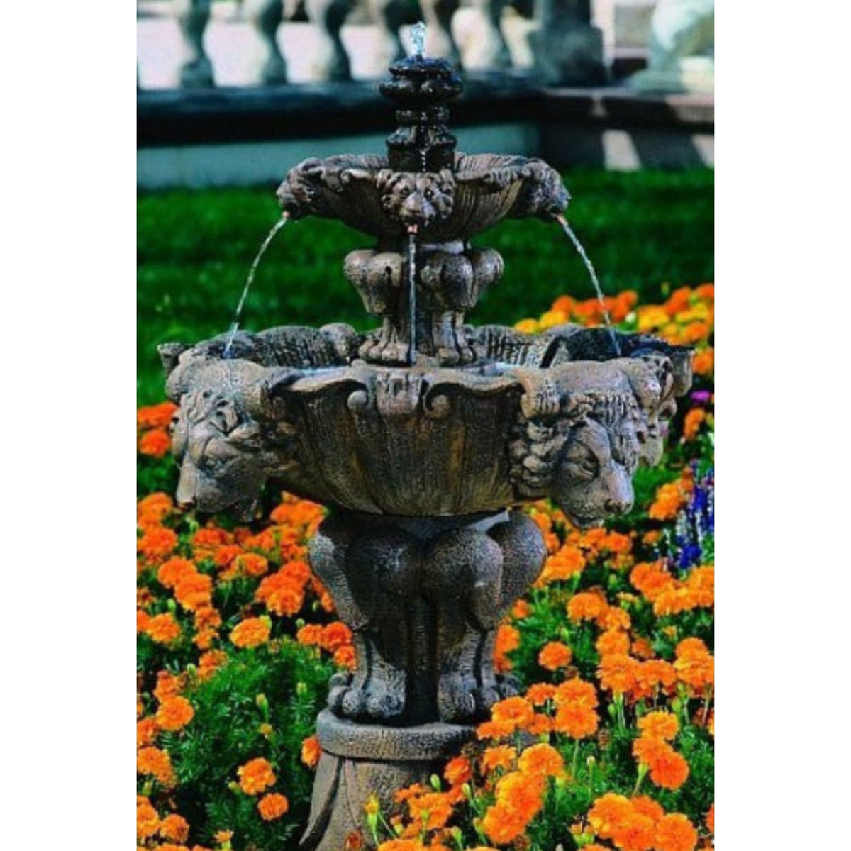 Fiore Stone small lion tiered cast stone fountain running in a garden bed edged with orange flowers