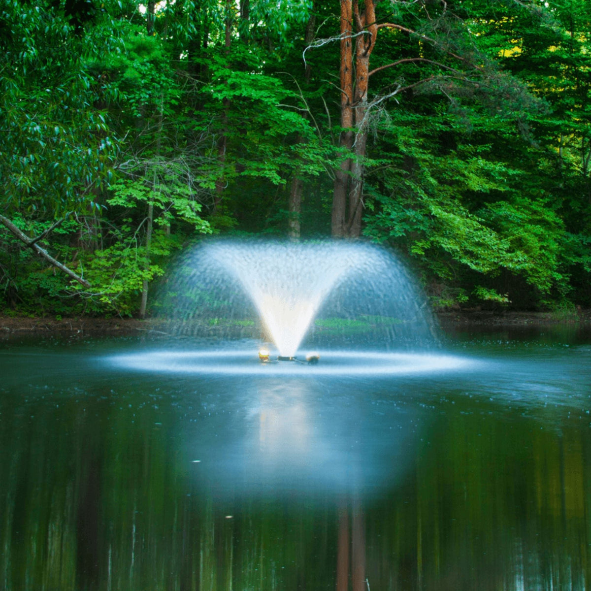 A Scott Aerator DA-20 throwing a lit spray on an open pond with green trees behind it