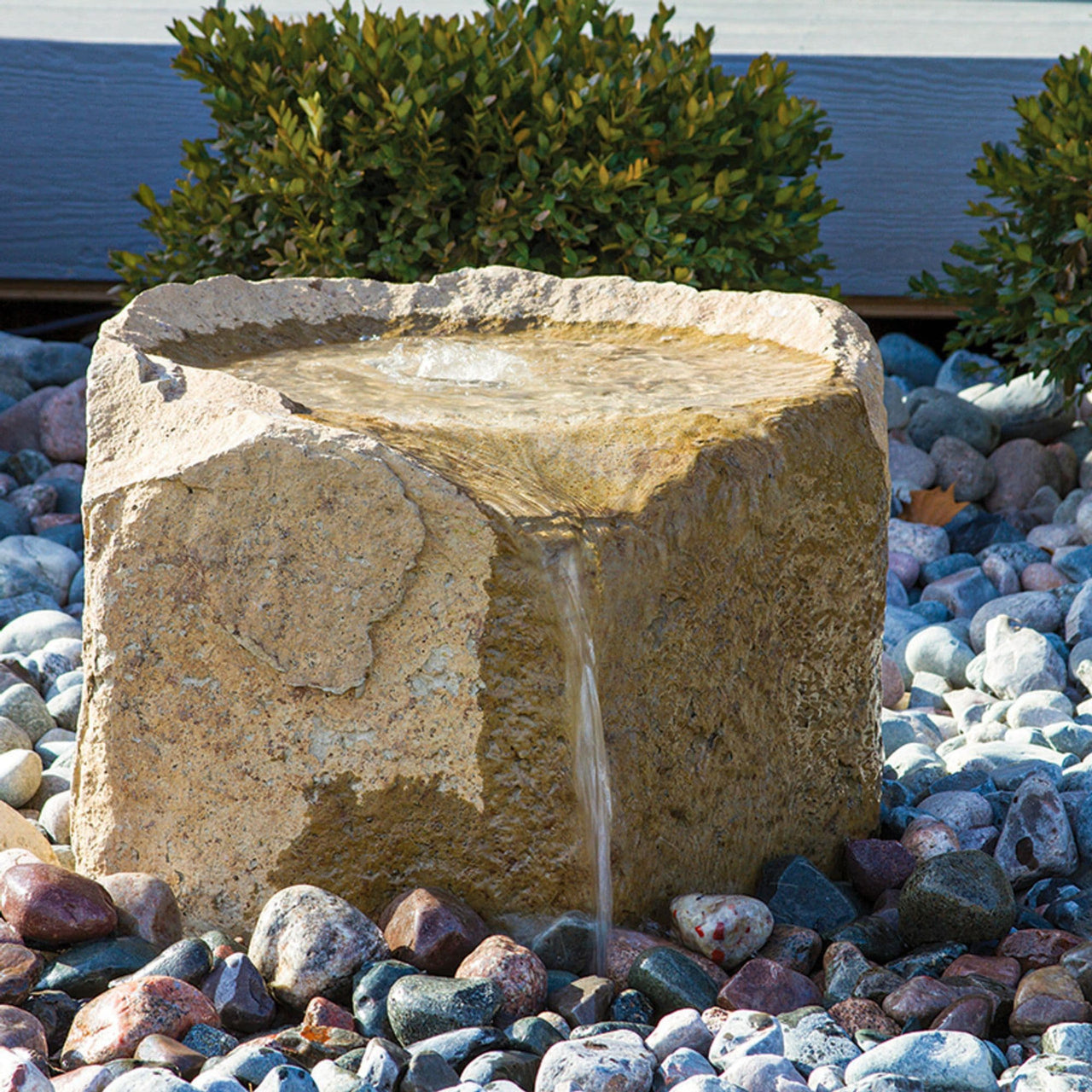 Alder Falls Rock Outdoor Fountain Surrounded By Stones With Small Trees In The Back