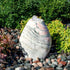 Thumbnail for Almond-Shaped Pink Marble Stone Fountain With  Small Trees Or Plants In The Background And Surrounded By Stones