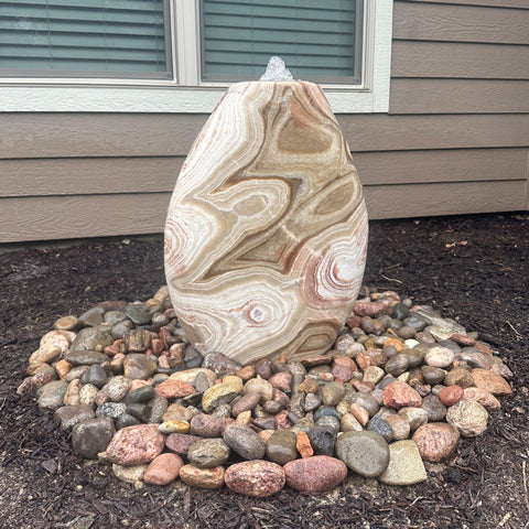 Almond-Shaped Red Onyx Stone Fountain With Window And Wooden Wall In The Background