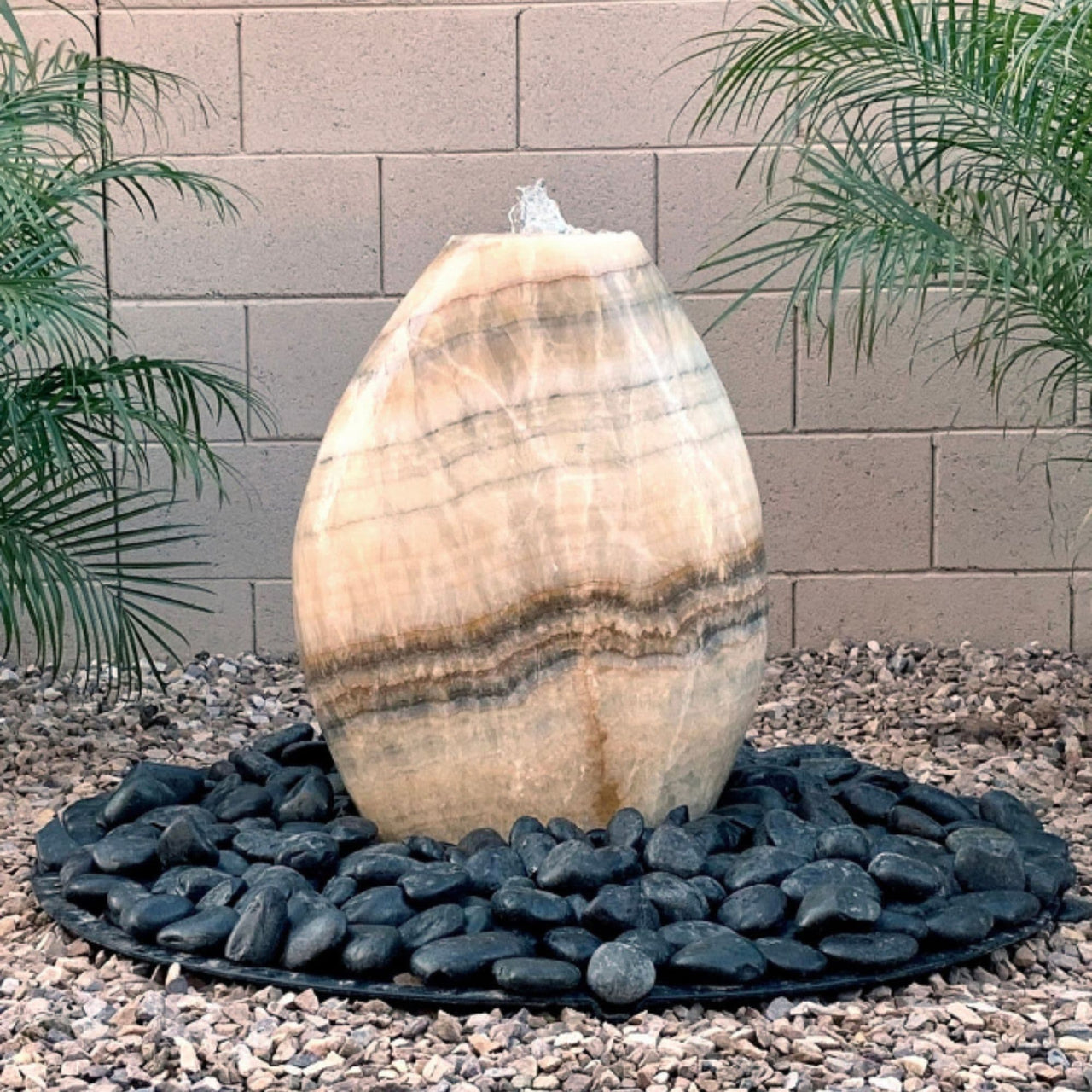 Almond-Shaped Yellow Onyx Stone Fountain With Brick Wall Background