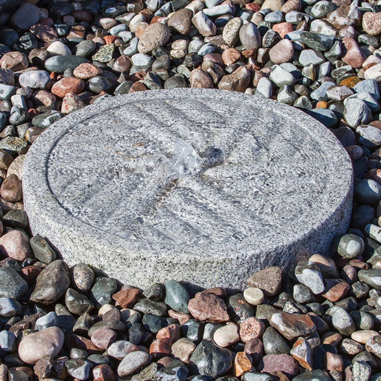 Angled Millstone Granite Stone Fountain Surrounded By Colorful Garden Stones