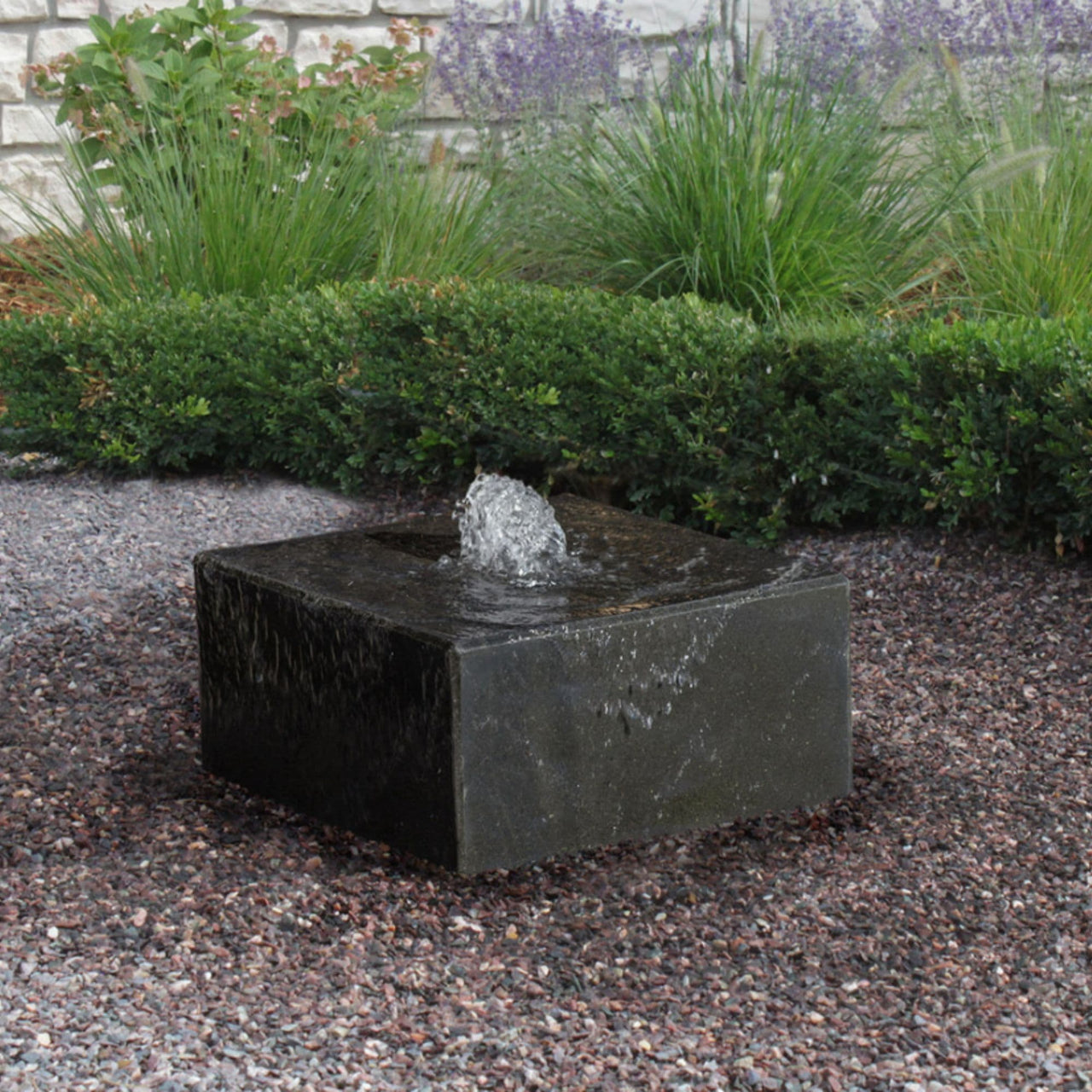 Basalt Garden Fountain With Green Plants And Brick Wall In The Background