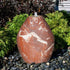 Thumbnail for Blue Thumb Almond-Shaped Red Marble Stone Fountain With  Small Trees Or Plants In The Background And Surrounded By Stones