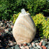 Thumbnail for Blue Thumb Almond-Shaped Yellow Onyx Stone Fountain With  Small Trees Or Plants In The Background And Surrounded By Stones