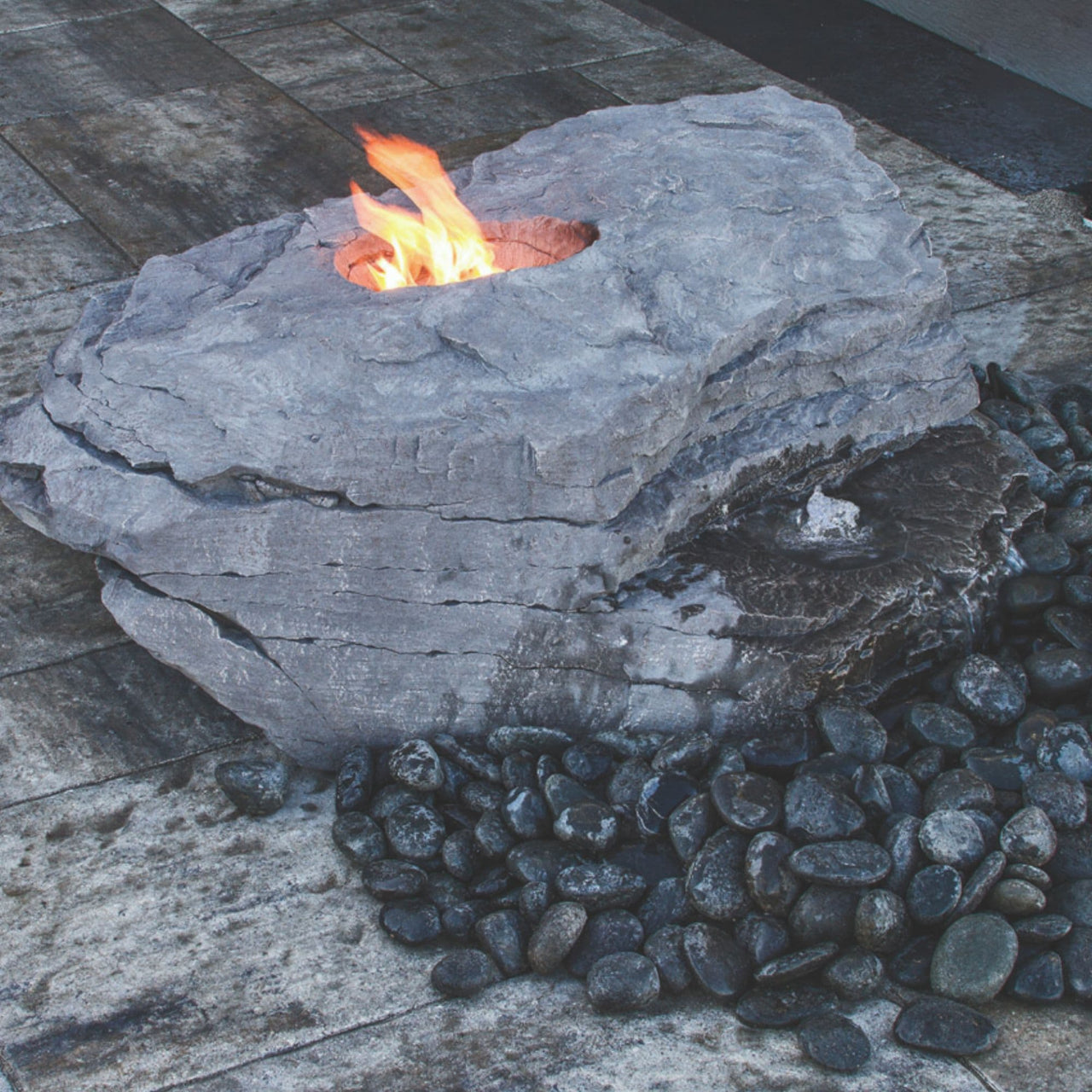 Blue Thumb Boulder Outdoor Fire Stone Fountain With A Fire And Surrounded by Black Pebbles