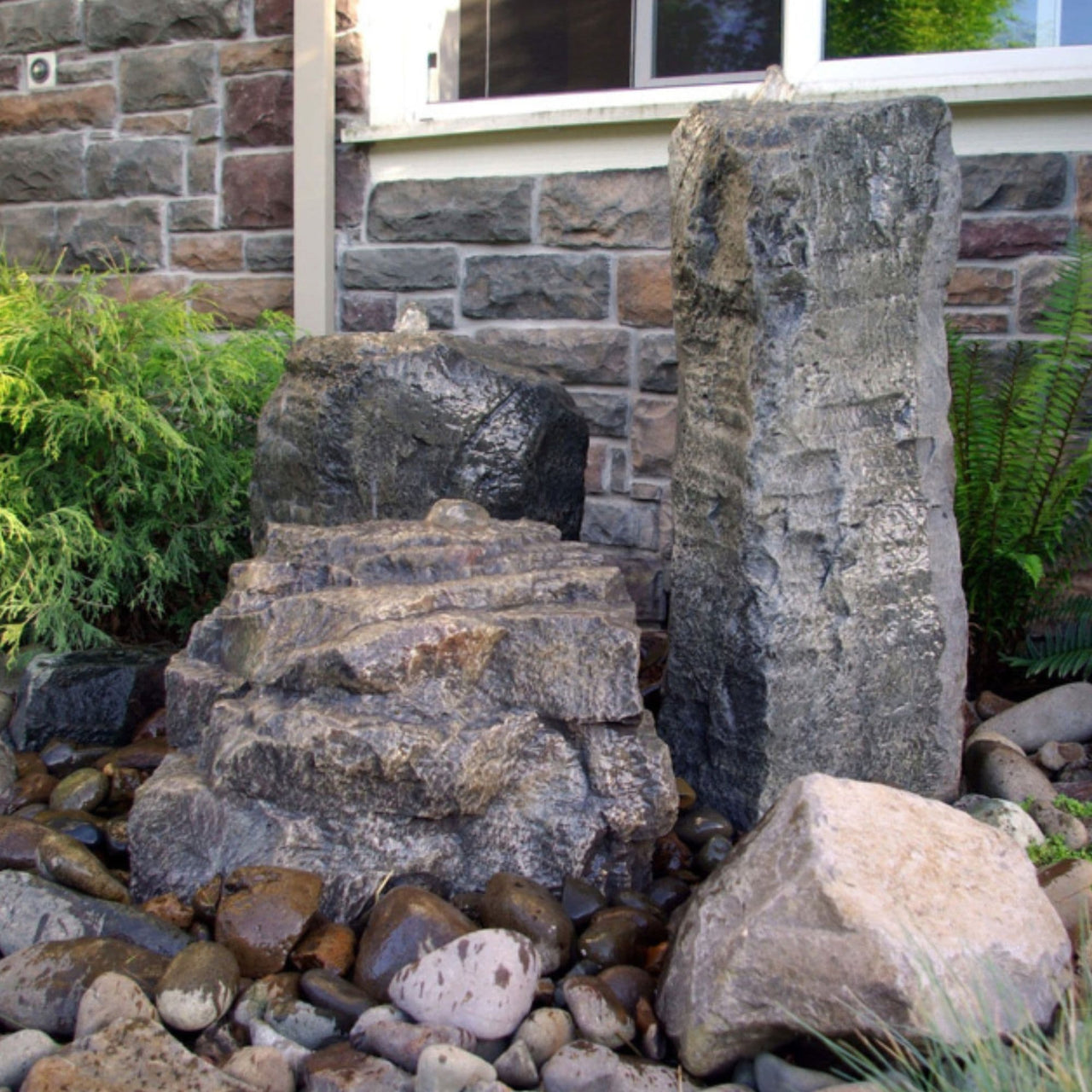 Blue Thumb Cascade Mini-Mountain Spring Triple Stone Outdoor Fountain With Brick Wall, Window, And Plants In The Background