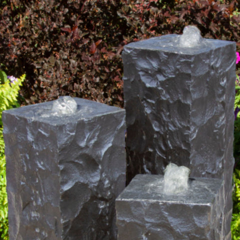 Blue Thumb Chiseled Black Basalt Column Outdoor Fountain With Different Plants In The Background