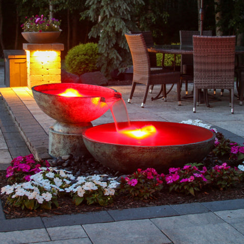 Blue Thumb Double Spillway Stone Bowl Fountain Surrounded By Plants Pink And White Flowers With Table And Chairs In The Background