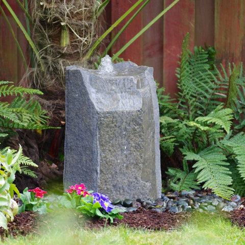 Blue Thumb Hollow Springs Garden Rock Fountain Surrounded By Plants And Flowers With Wooden Wall Background
