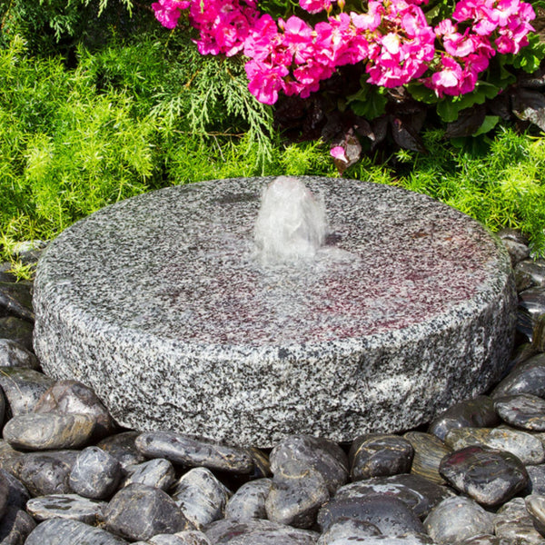Blue Thumb Natural Round Granite Stone Fountain With Vibrant Color Flowers And Shrubs Plants Behind
