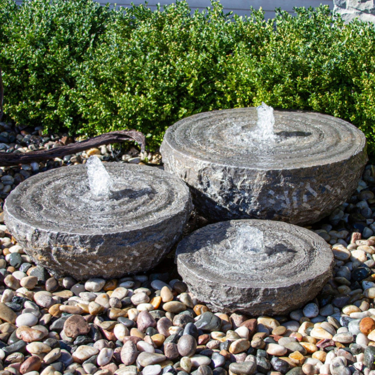 Blue Thumb Natural Stone Bowl with Swirl Fountains - Set of 3 Surrounded By Pebbles With Green Plants Behind
