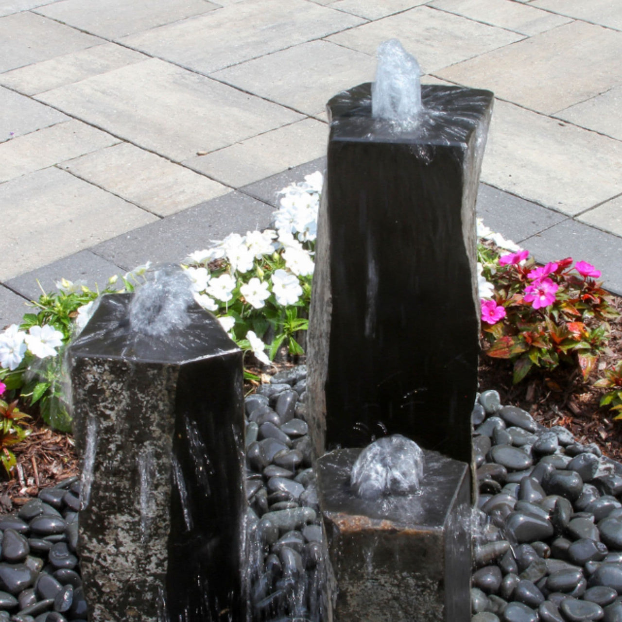 Blue Thumb One Side Polished Basalt Stone Fountain Slightly Top View With White And Pink Flowers Behind
