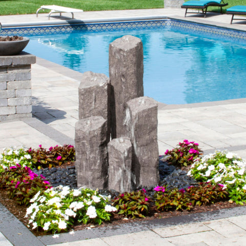 Blue Thumb Pent 5 Column Stone Faux Basalt Fountain Color Gray Surrounded By Colorful Flowers With Pool In The Back