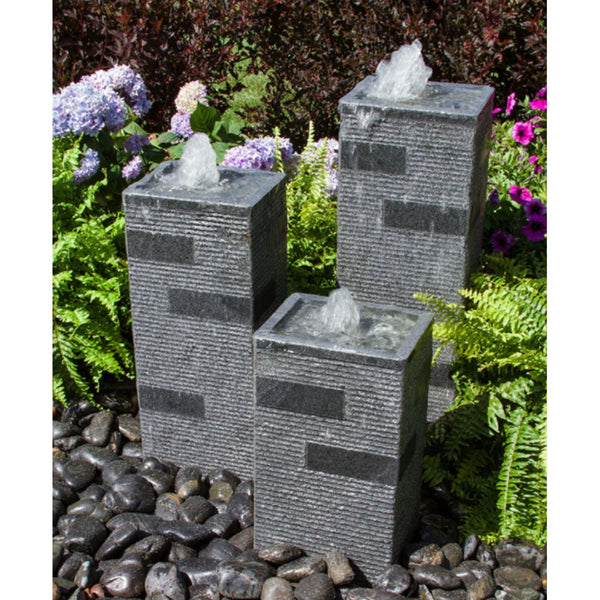 Blue Thumb Polished Block Stone Towers Outdoor Fountain Surrounded By Ferns And Flowers With Red Trees Behind