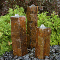 Thumbnail for Blue Thumb Polished Top Basalt Rock Column Fountain Besides Bushes With Red Trees Behind
