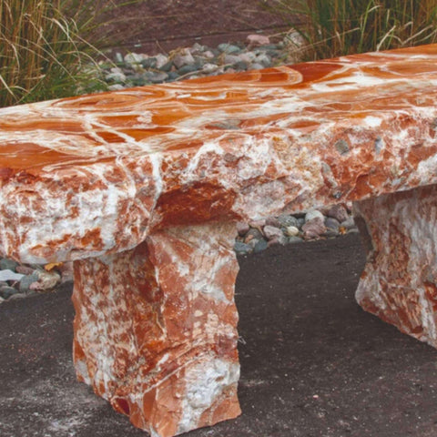 Blue Thumb Red Onyx Garden Bench Close-up View Near Brown Wall With Pebbles And Tall Grasses