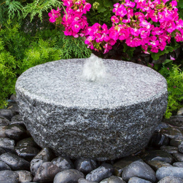 Blue Thumb Ringed Circle Granite Stone Fountain With Shrubs And Pink Flowers Backdrop