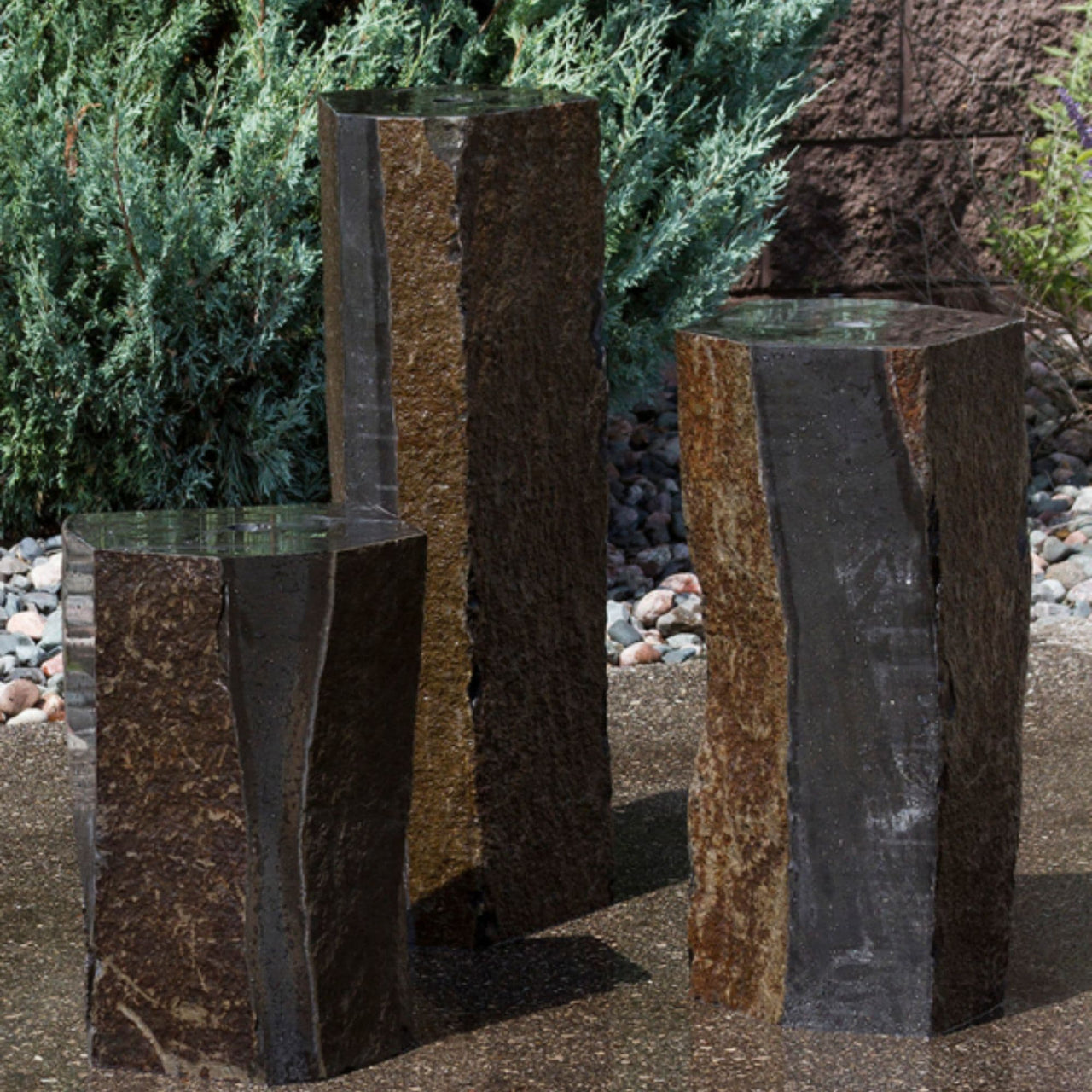 Blue Thumb Semi-Polished Basalt Rock Column Fountain With Shrubs Plants Behind