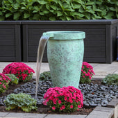 Blue Thumb Single Round Urn Fountain Surrounded By Red Flowers With Big Planters And a Green Plants In The Back