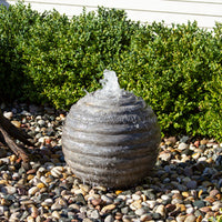 Thumbnail for Blue Thumb Smooth Ribbed Limestone Sphere Stone Fountain Surrounded By Green Plants With White Wall