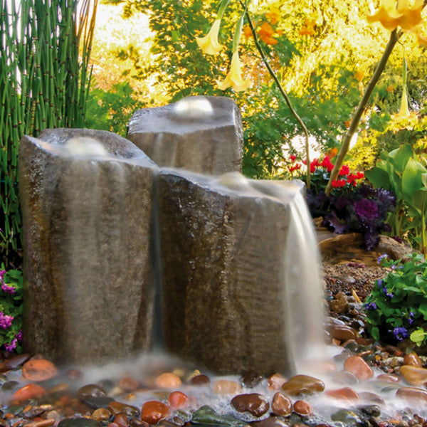 Blue Thumb Triple Column Outdoor Fountain Rocks With Colorful Flowers And Green Plants Background