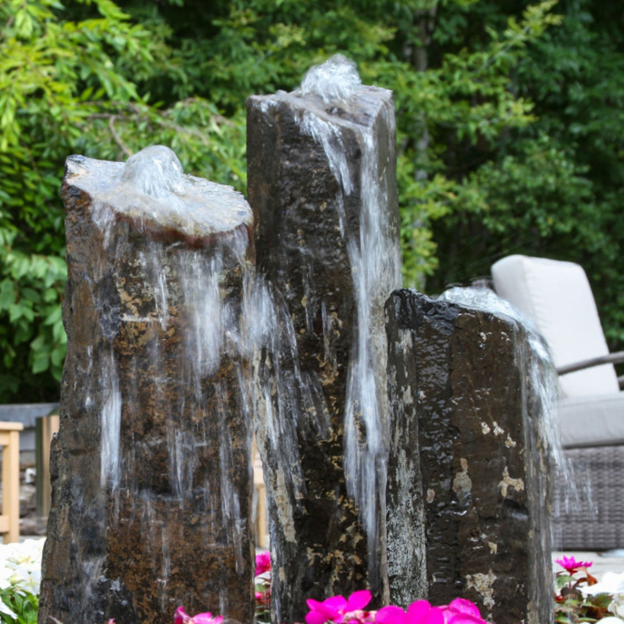 Blue Thumb Triple Rustic Basalt Stone Outdoor Fountain With Green Trees And Chair Background