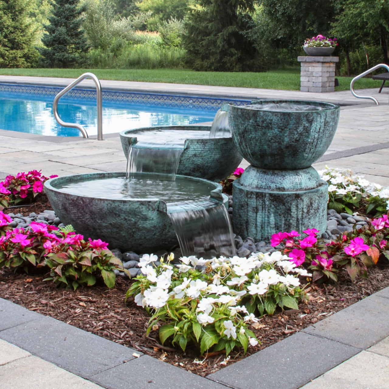 Blue Thumb Triple Spillway Stone Bowl Fountain Surrounded By Flowers With A Pool  Background