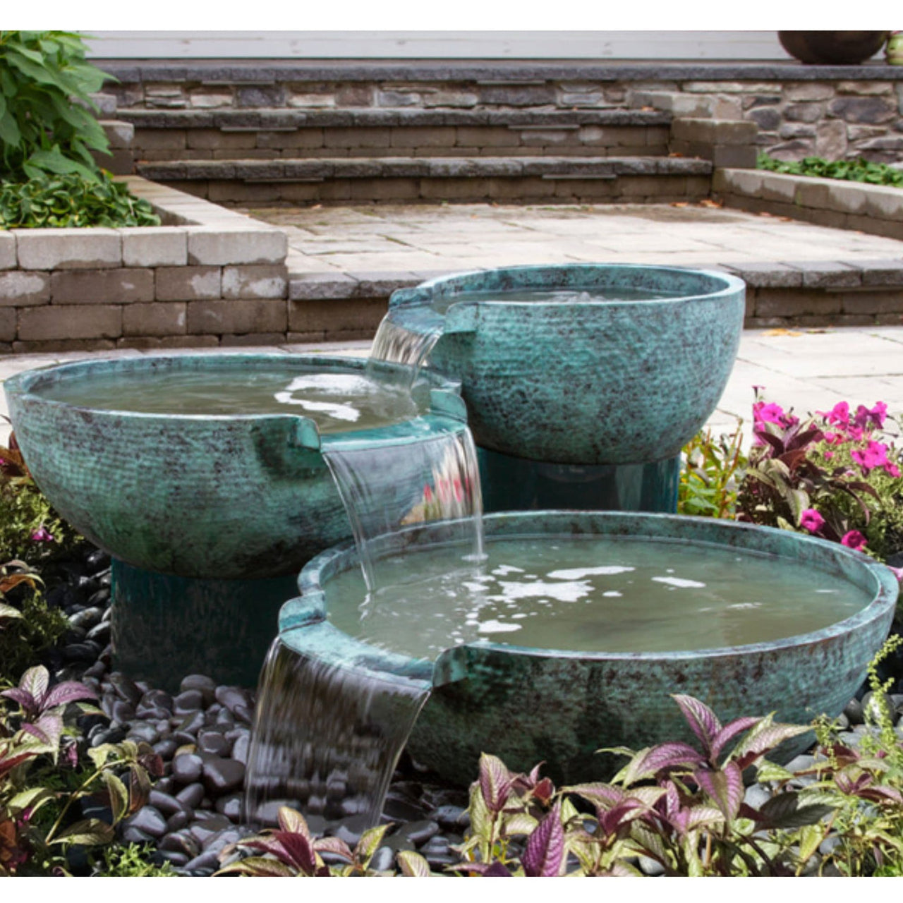 Blue Thumb Triple Spillway Stone Bowl Fountain Surrounded By Flowers With Paved Pathway