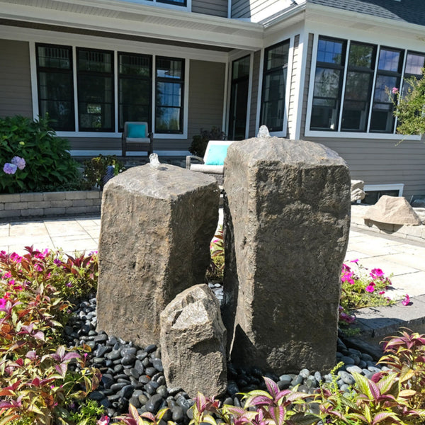 Blue Thumb Watershed Tall Double Rock Outdoor Fountain Surrounded By Colorful Plants With A Modern House In The Background