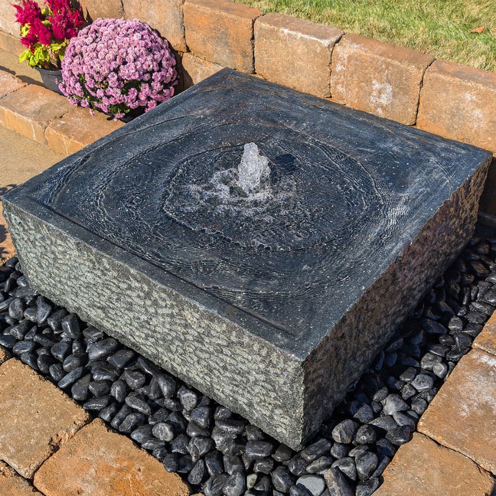 Blue Thumb Yoshida Square Stone Fountain On Black Pebbles With Flowers In The Background