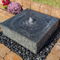Thumbnail for Blue Thumb Yoshida Square Stone Fountain On Black Pebbles With Flowers In The Background