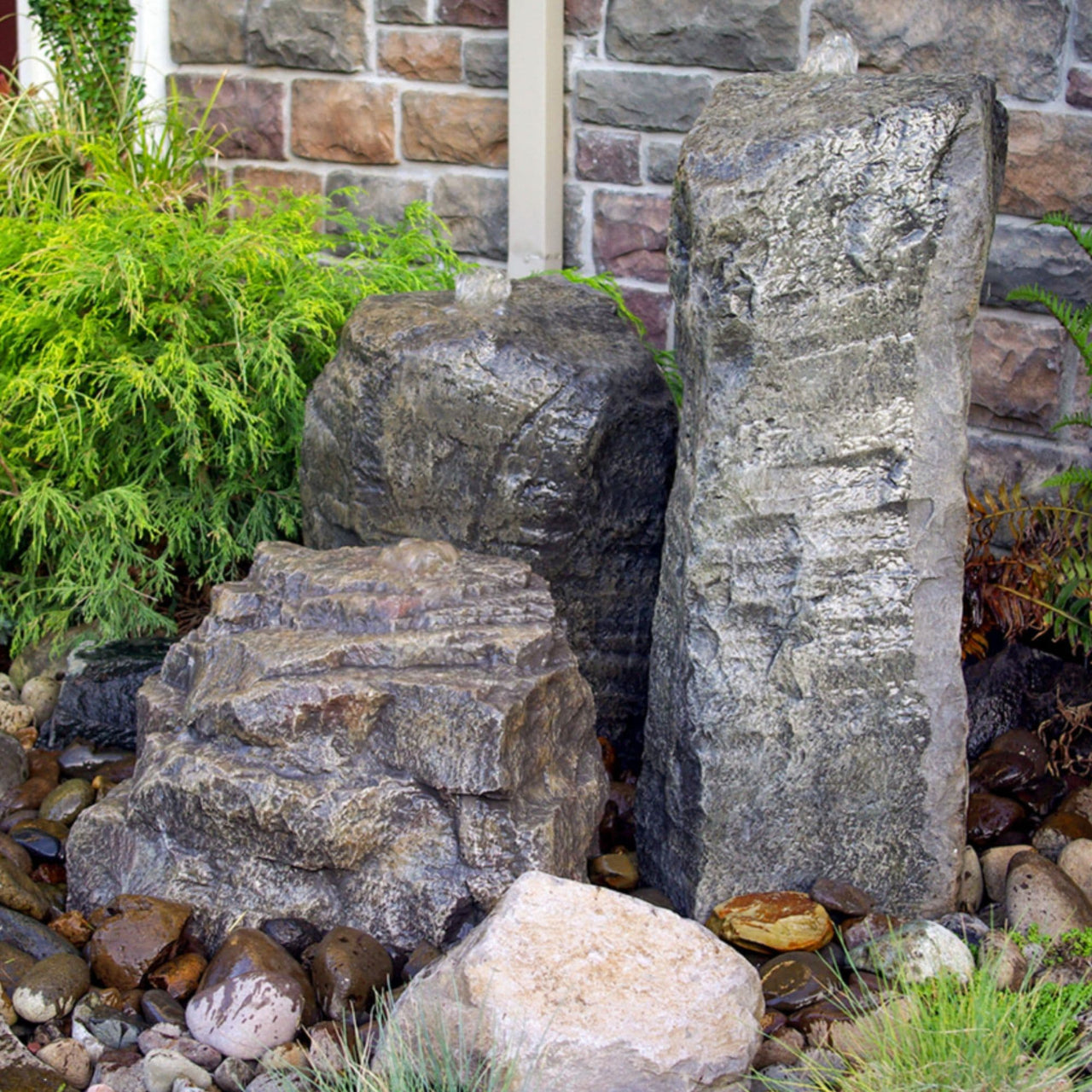 Cascade Triple Stone Outdoor Fountain With Brick Wall And Plants In The Background