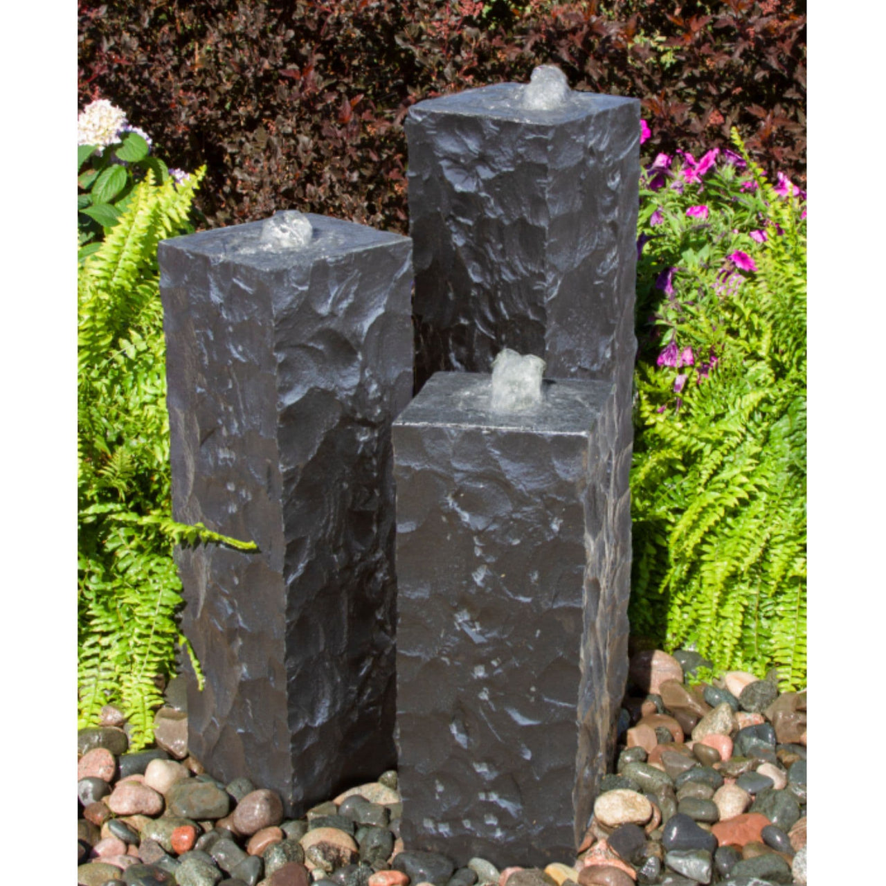 Chiseled Black Basalt Column Outdoor Fountain With Different Plants In The Background