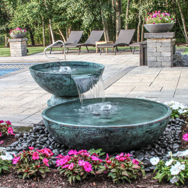 Double Spillway Stone Bowl Fountain Surrounded By Pink And White Flowers  With Pool In The Background