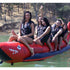 Thumbnail for Elite Class 6 Person Red Shark Banana Boat With A Group Having Fun And Excited For A Ride With A Forested Hillside in the Background