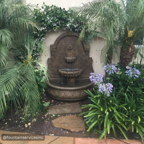 Fiore Stone Bavarian Wall Fountain Besides Purple Flower and Palm Trees