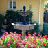 Thumbnail for Giannini Garden Appia Antica Two Tier Lion Outdoor Water Fountain With Red Flowers In The front And A House In The Background