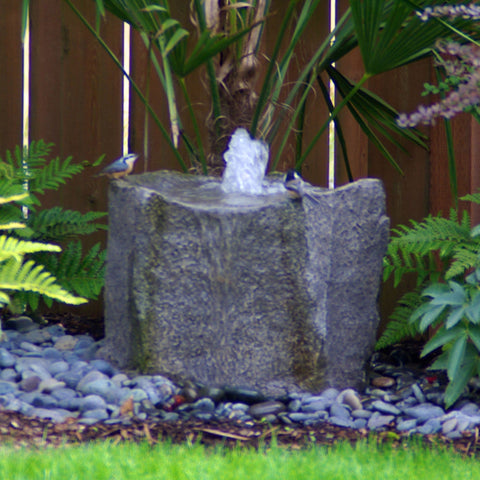 Klamath Basin Stone Outdoor Fountain Surrounded By Green Plants And Wooden Fence Behind