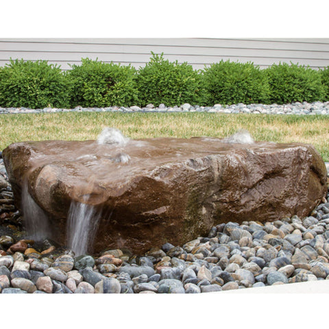 Manistique Falls Stone Outdoor Fountain On Pebble And Grass Bed With Green Shrub Backdrop