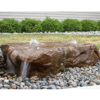 Thumbnail for Manistique Falls Stone Outdoor Fountain On Pebble And Grass Bed With Green Shrub Backdrop